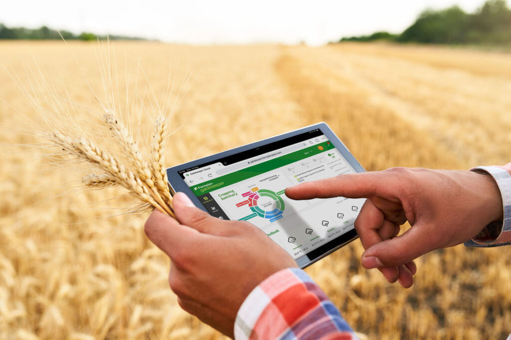 close up of hands holding a tablet with graphs on it, with a wheat field in the background of the image.